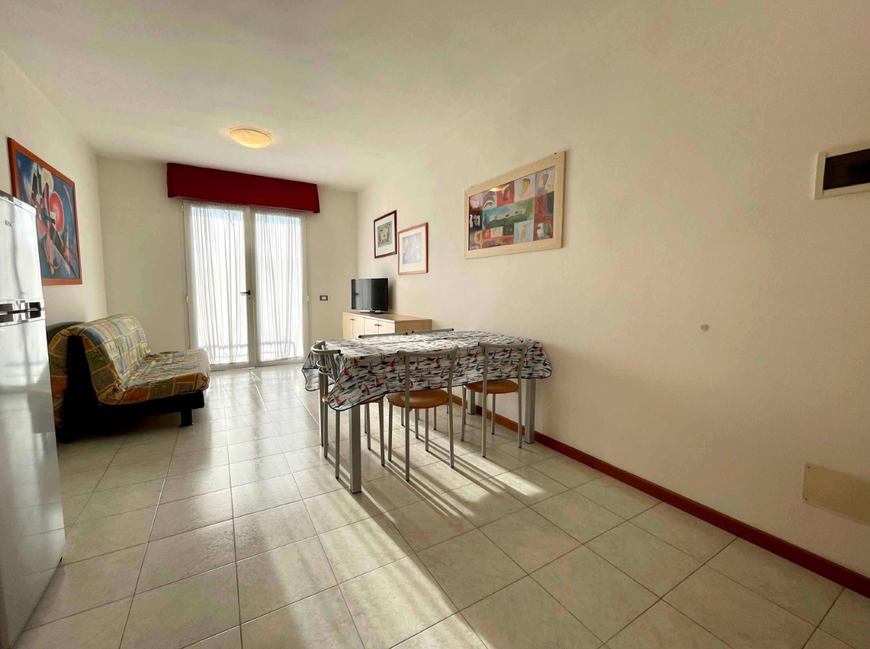 A dining area with a table and chairs, a sofa, a television, and artwork on the walls.