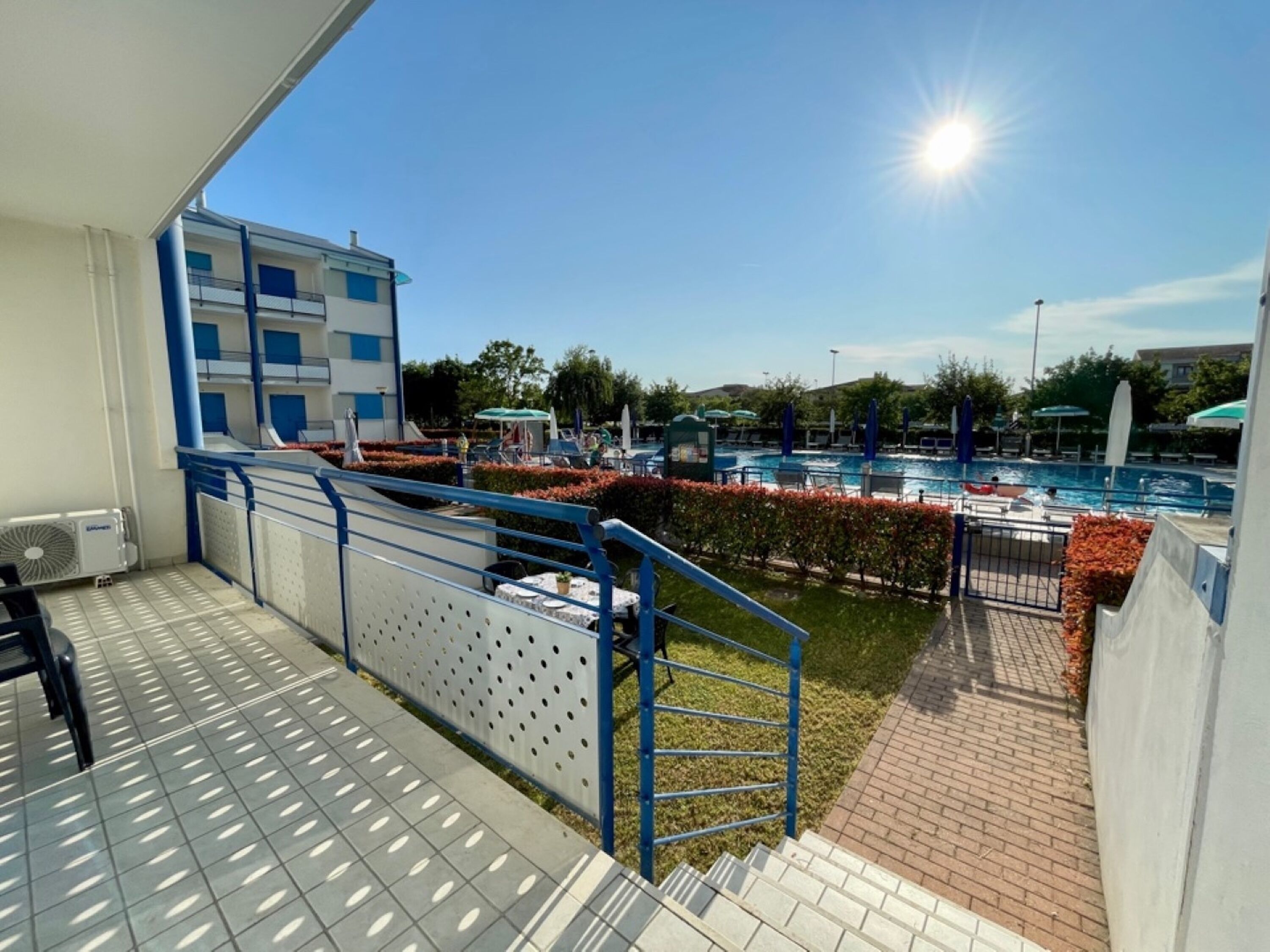 Un balcón con vista a la piscina, una escalera y un edificio de color azul y blanco.