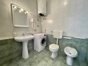 A bathroom with a sink, washing machine, toilet, bidet, and a mirror with lights. - The Perfect Home Base for Your Beach Vacation (Caorle)