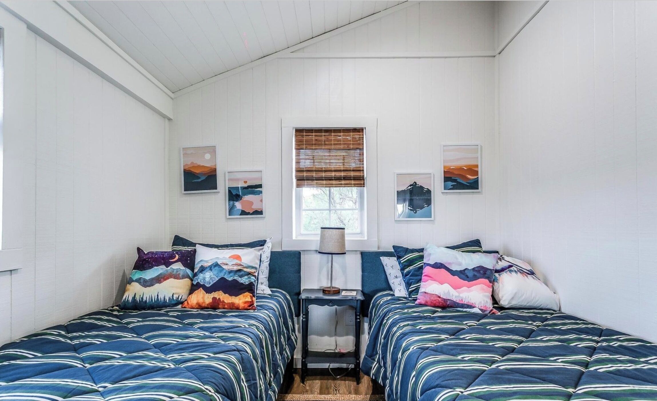 A bedroom with two beds, a nightstand, and a window with blinds.