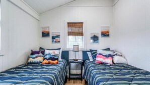 Un dormitorio con dos camas, una mesita de noche y una ventana con persianas.