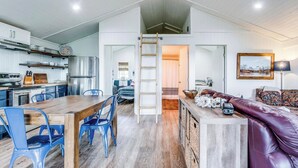 Amplio espacio tipo loft con zona de comedor, sillas azules, banco de madera y habitación superior a la que se accede por una escalera.