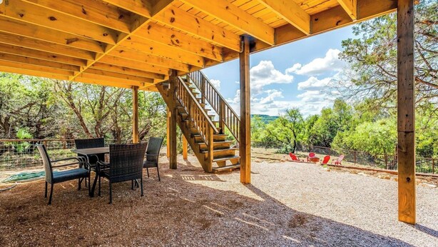 Un espacio exterior cubierto con una escalera de madera que conduce a un nivel superior, rodeado de árboles y suelo de grava.