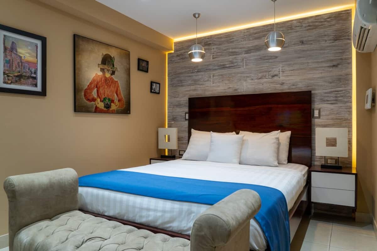 A hotel room with a large bed, two bedside tables, a headboard, and a painting on the wall.