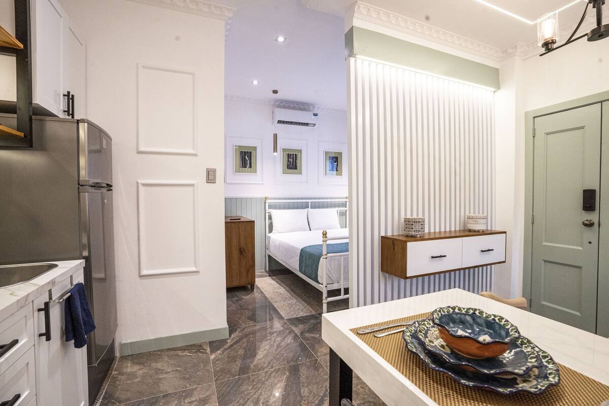 A modern kitchen with a stainless steel refrigerator, a wooden cabinet, and a dining area with a table and decorative bowl.