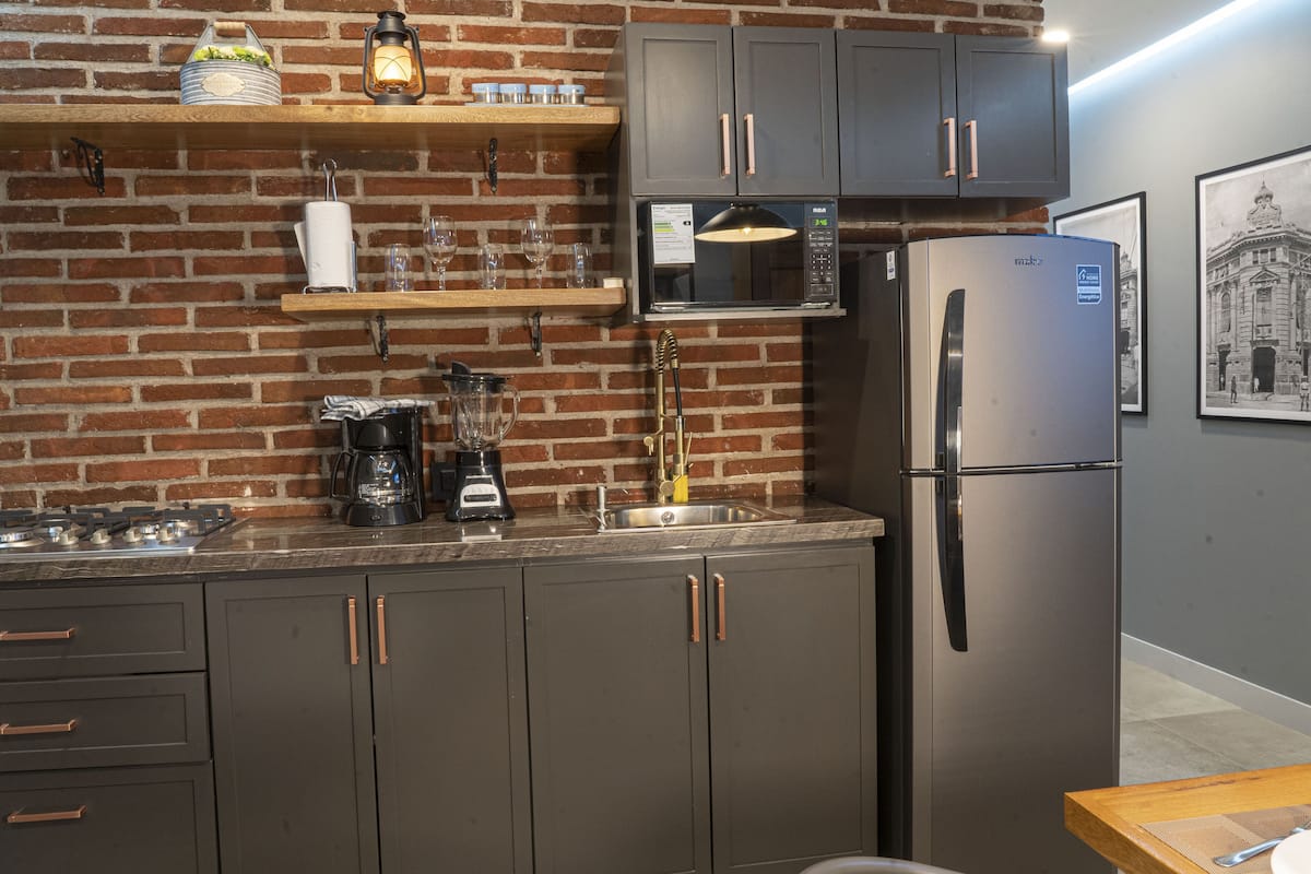 A kitchen with a brick wall, a microwave, a refrigerator, and a coffee maker.