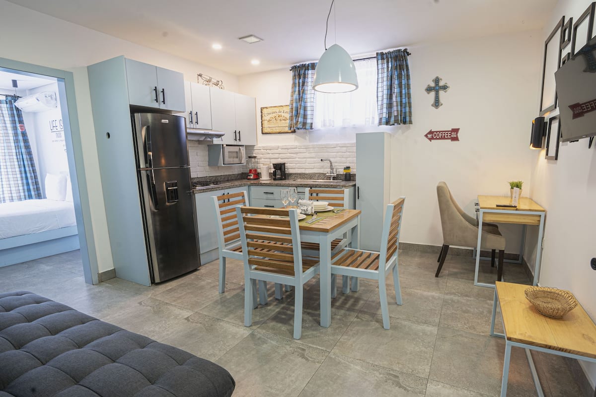 A modern kitchen with a refrigerator, stove, and dining area. There is a coffee sign on the wall and a cross decoration.