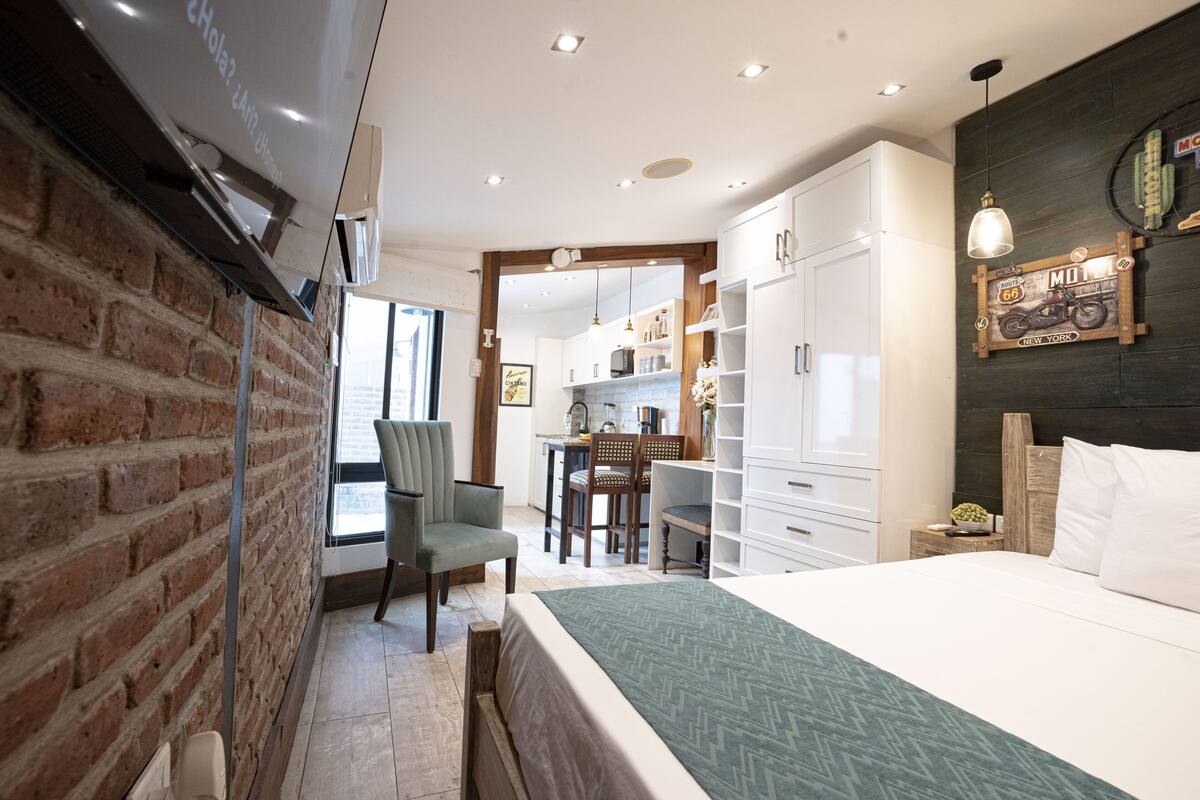 A bedroom with a brick wall, a bed, a desk, and a chair.