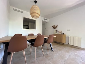Un comedor con mesa de madera y sillas marrones, una lámpara colgante de fibras, un aparador con objetos decorativos y un radiador en la pared.