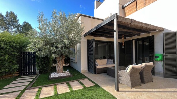 Um pátio moderno ao ar livre com pérgola, área de estar e uma árvore.