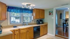A kitchen with wooden cabinets, a dishwasher, a coffee maker, and a window with blinds. - Waycross Vacation Rental w/ Private Backyard! (Waycross)