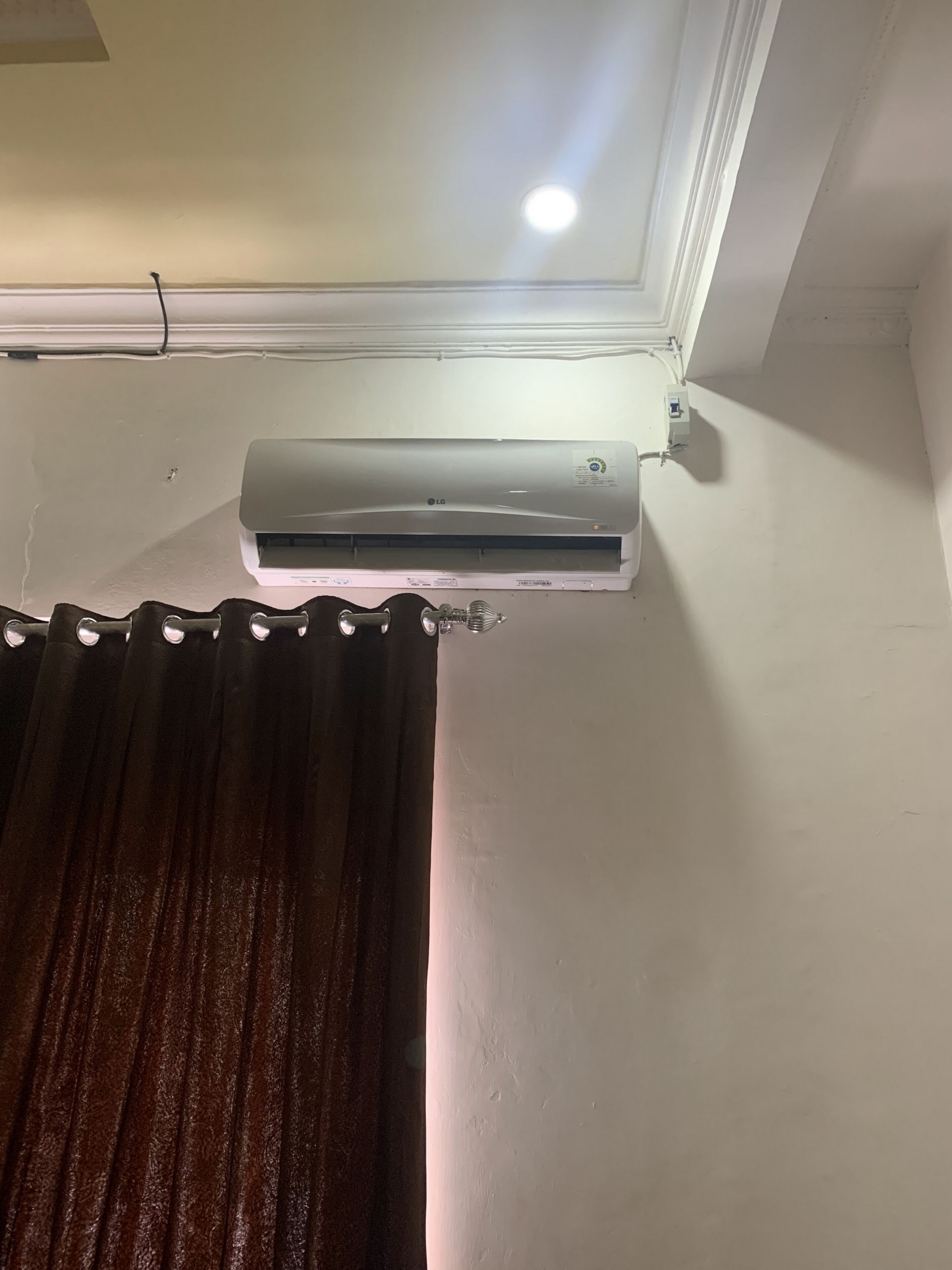 Un appareil de climatisation fixé au mur, avec une prise de courant visible et un luminaire au plafond.