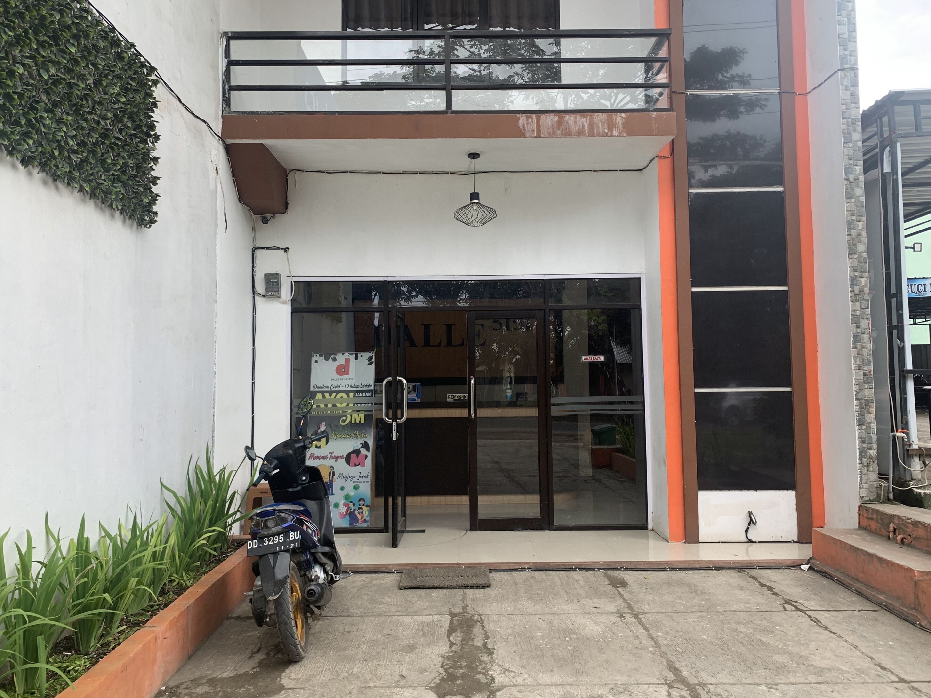 A building entrance with a motorcycle parked in front, a glass door, and a small garden area with plants.