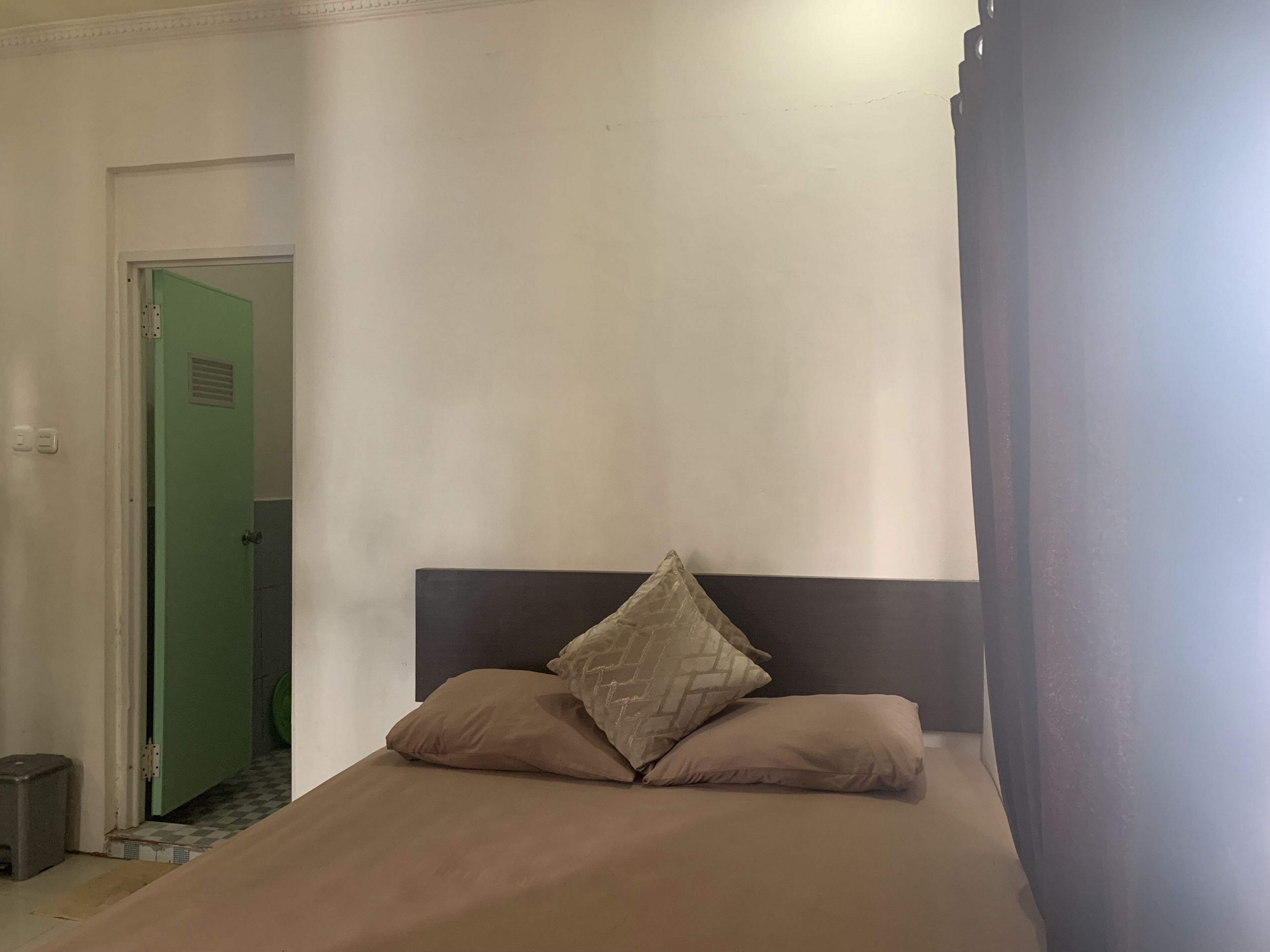A bedroom with a single bed, a green door, and a tiled floor.