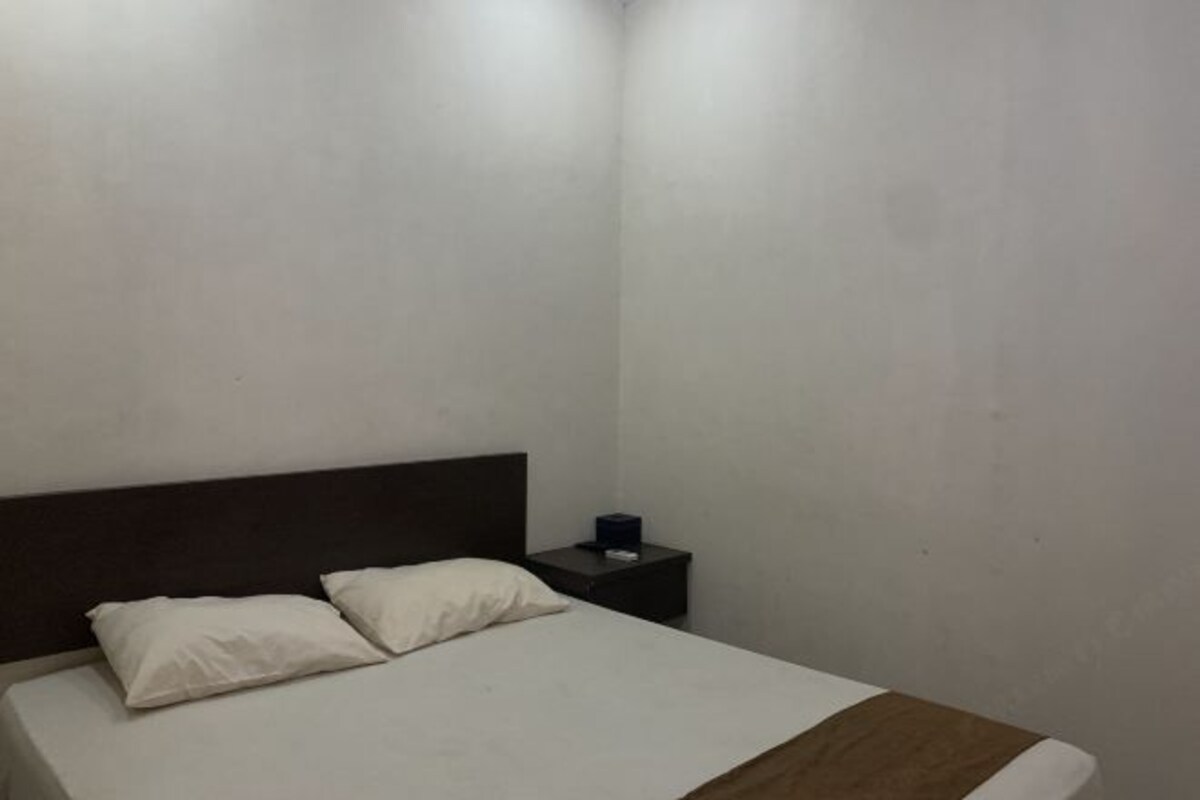 A small, simple room with a single bed, a nightstand, and a plain wall.