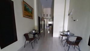 Un couloir avec deux tables rondes et des chaises, un tableau au mur et une porte sur la gauche.