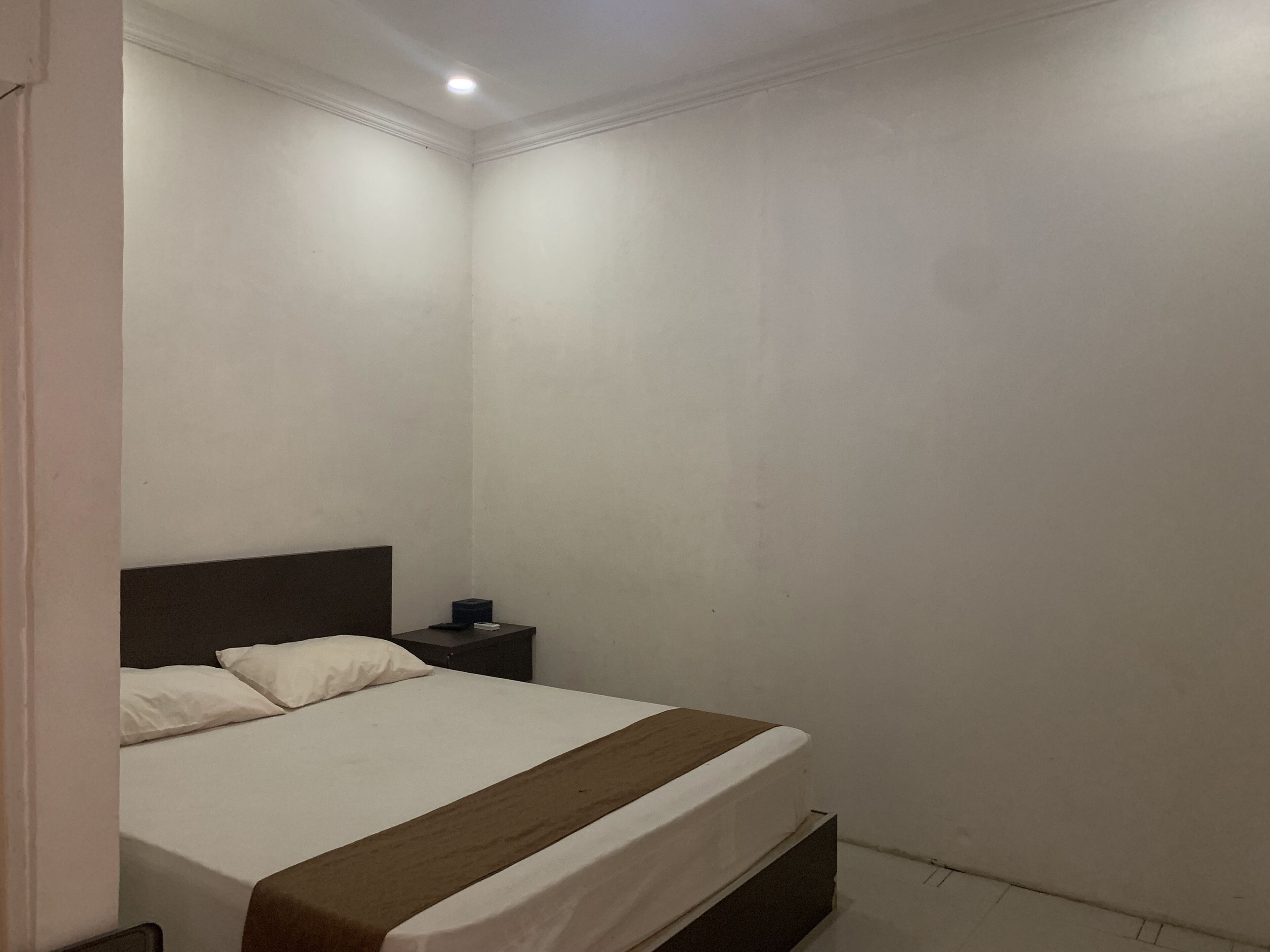 Un dormitorio pequeño y sencillo con una cama individual, una mesita de noche y una lámpara de pared.