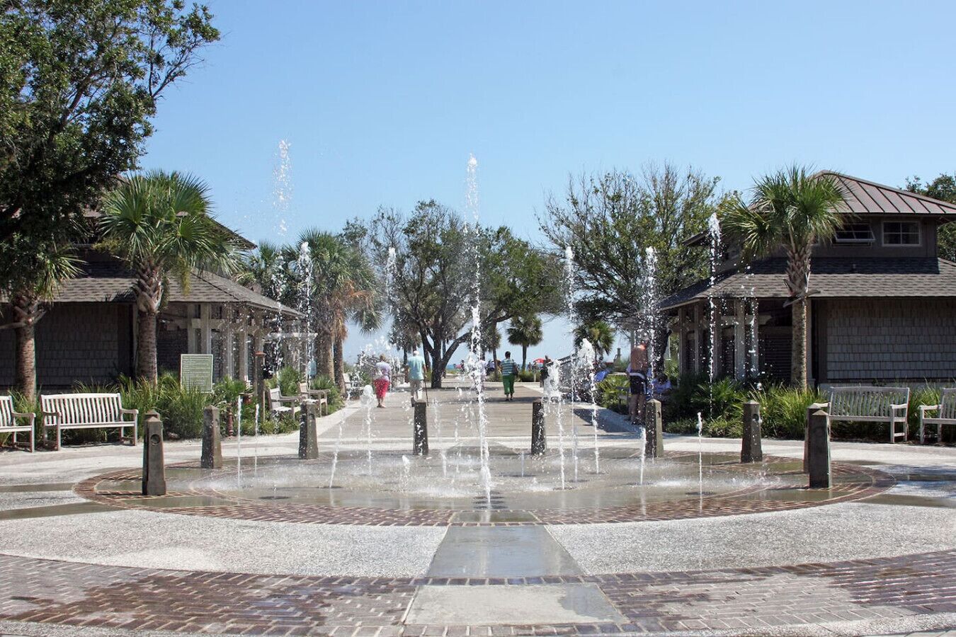 A public square with a central water feature, benches, and palm trees.