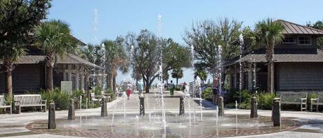 A public square with a central water feature, benches, and palm trees.