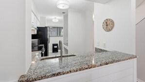 Een moderne keuken met granieten aanrechtbladen, roestvrijstalen apparatuur en een klok aan de muur.