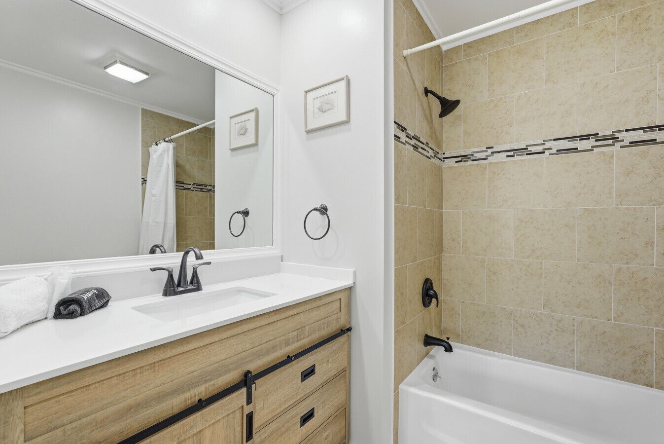 Een badkamer met een grote spiegel, een wastafel, een wastafelmeubel met lades, een douche en een bad.