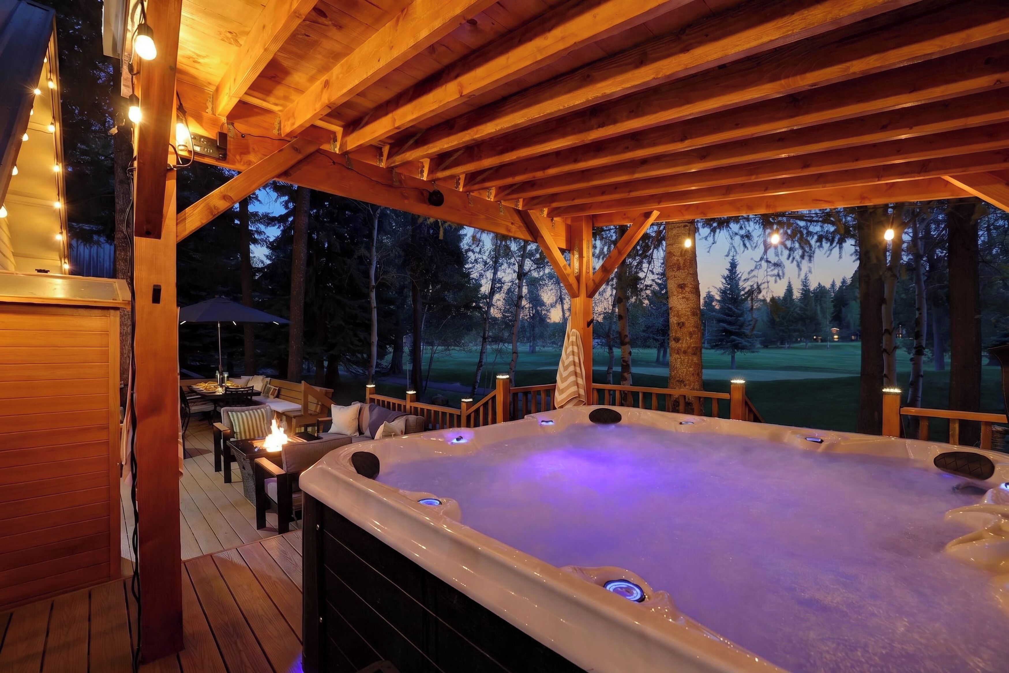 Un bain à remous installé sous une terrasse en bois, offrant une vue sur un terrain de golf au crépuscule.