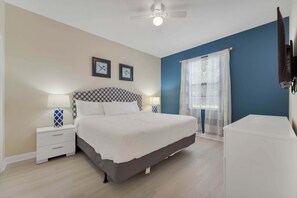 A bedroom with a bed, nightstands, a ceiling fan, a TV, and a window with curtains. - 8BR Champions Gate Pool Home | 5 King Beds | Theater Room | Dog Friendly (Champions Gate)