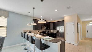 A modern kitchen with a central island, bar stools, and pendant lighting. - 8BR Champions Gate Pool Home | 5 King Beds | Theater Room | Dog Friendly (Champions Gate)