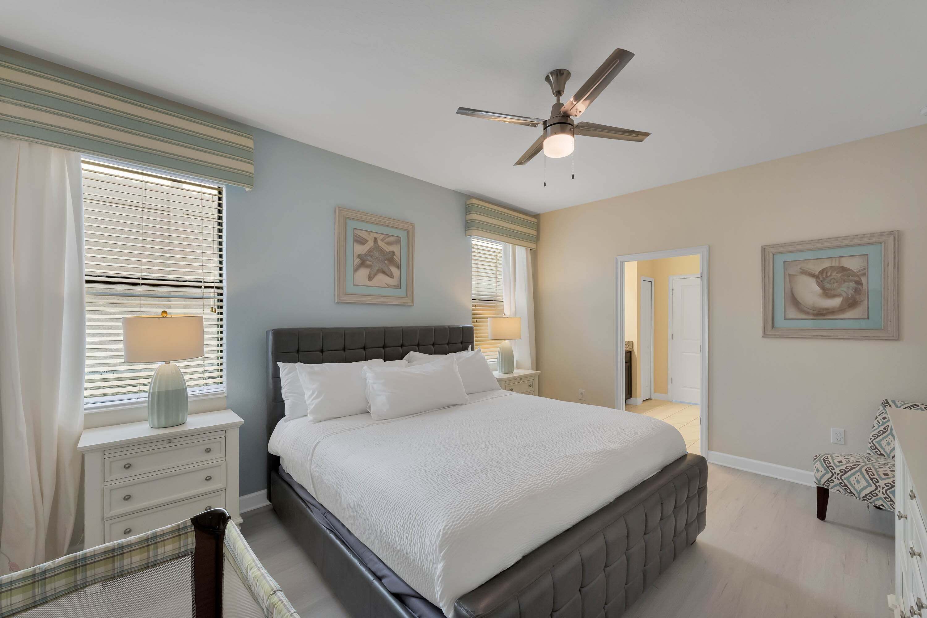 A bedroom with a bed, nightstands, a ceiling fan, and artwork on the walls.