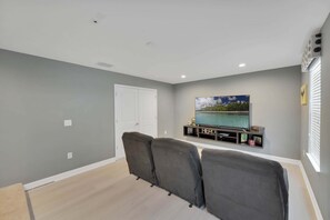 A living room with a flat-screen TV on a stand, grey walls, a white door, and a window with blinds. - 8BR Champions Gate Pool Home | 5 King Beds | Theater Room | Dog Friendly (Champions Gate)