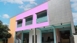 A two-story building with a pink and beige facade, a covered entrance with a staircase, and a balcony with a metal railing. - Hotel O Jayanni (Sumbawa Besar)