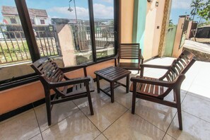 A sunlit patio with wooden furniture and a view of a residential area. - Hotel O Jayanni (Sumbawa Besar)