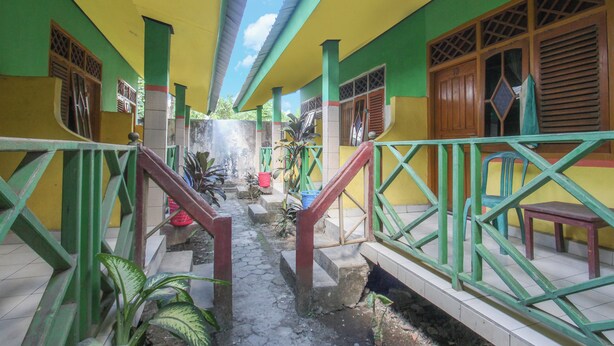 A corridor with green railings, a staircase, and a small garden area with plants and a red bucket. - Hotel O Jayanni (Sumbawa Besar)