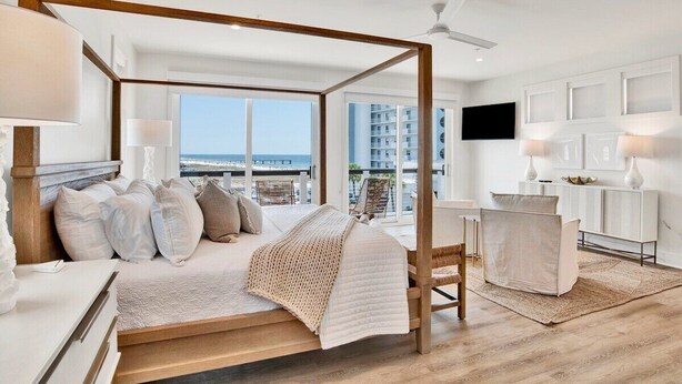Un dormitorio moderno con cama con dosel, vistas al océano y un balcón con panorama urbano.