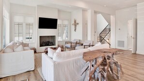 Una amplia sala de estar con chimenea, sofás blancos, una mesa de centro y una escalera que conduce a otro nivel.