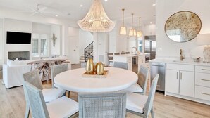 Una cocina moderna con armarios blancos, una mesa de comedor redonda, sillas de mimbre e iluminación colgante.