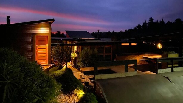 A modern house with a wooden exterior, a well-lit entrance, and a landscaped garden area. - Cabañas La Ola Puertecillo (Navidad)