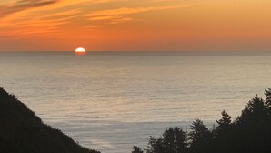 A sunset over a calm sea with a silhouette of trees in the foreground. - Cabañas La Ola Puertecillo (Navidad)