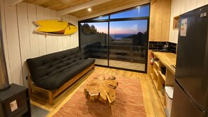 A modern kitchen with a large window, a black sofa, and a wooden coffee table. - Cabañas La Ola Puertecillo (Navidad)