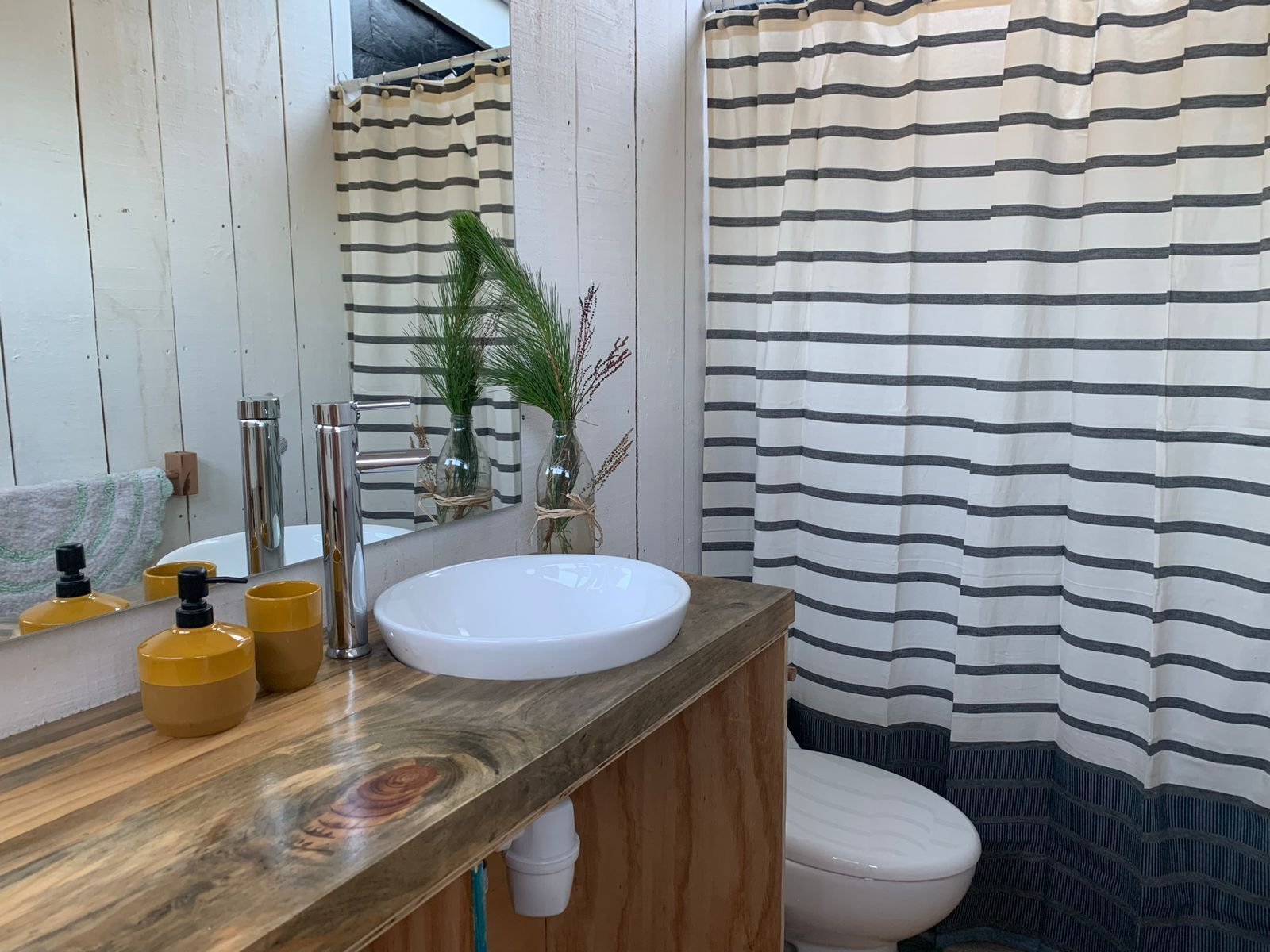 A bathroom with a wooden vanity, a white sink, a mirror, and a striped shower curtain.