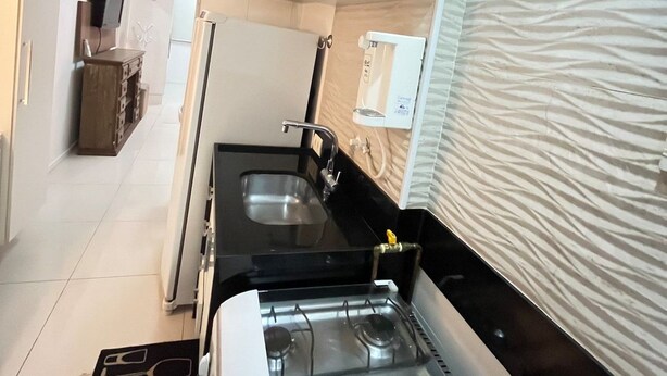 A compact kitchen with a gas stove, two sinks, and white cabinets. - Stúdio Praia Ipanema (Rio de Janeiro)