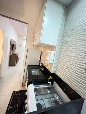 A compact kitchen with a gas stove, two sinks, and white cabinets. - Stúdio Praia Ipanema (Rio de Janeiro)