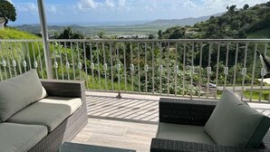 Un balcón con mobiliario de mimbre y vistas a un paisaje verde.