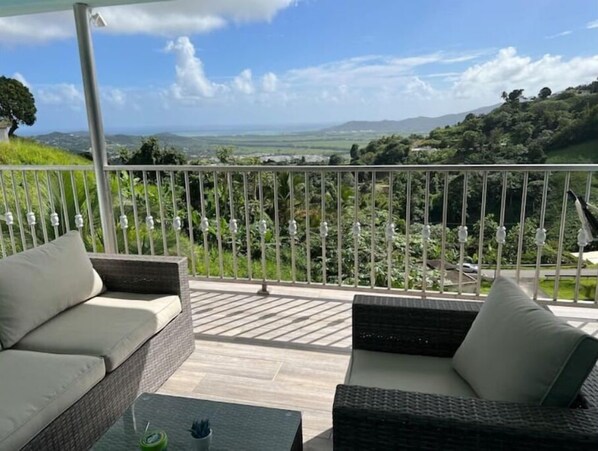 A balcony with wicker furniture and a view of a green landscape.