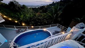 Zona de piscina amb banyera hidromassatge, envoltada d'una barana blanca, amb vista a un paisatge verdós ple d'arbres i turons allunyats.