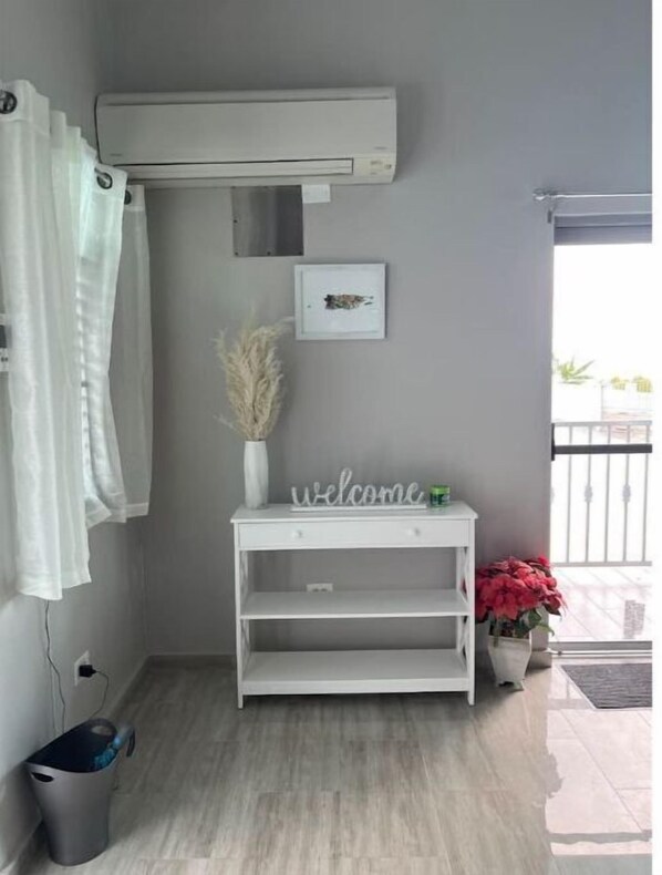 A small, clean room with a white air conditioning unit, a welcome sign, a potted plant, and a window with a view. - Modern Retreat w/ Great View, Hot Tub, & Pool (Yabucoa)