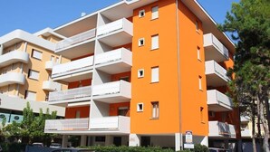 A multi-story building with balconies, a parking area, and greenery. - Homely Flat few Minutes From the Beach - Beahost (San Michele al Tagliamento)