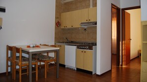 A compact kitchen with wooden cabinets, a built-in oven, and a dining area with a table and chairs. - Homely Flat few Minutes From the Beach - Beahost (San Michele al Tagliamento)