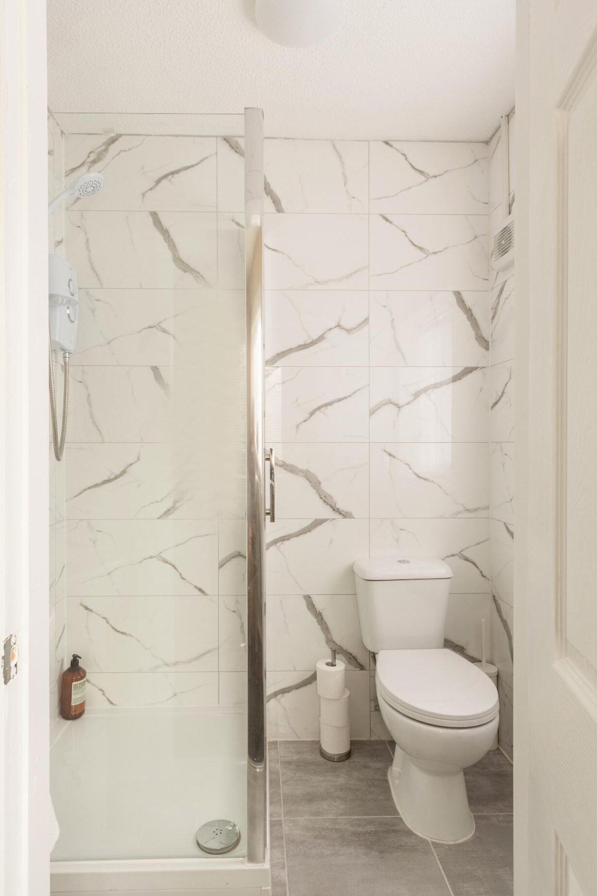 A bathroom with a shower, toilet, and marble-patterned walls.