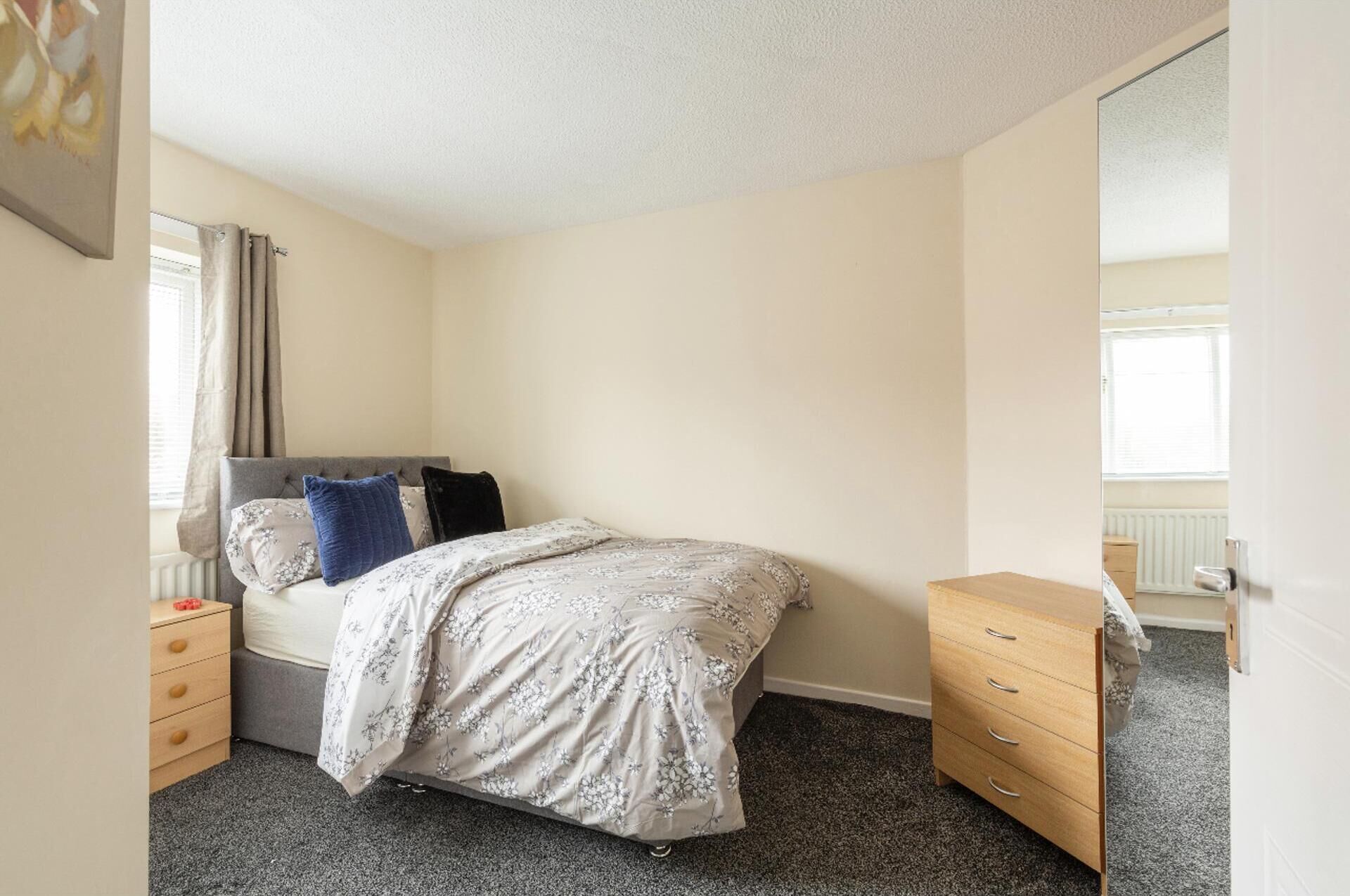 A bedroom with a bed, a dresser, a nightstand, and a window with curtains.